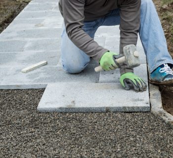 worker hammering the stone plates to install footpath at garden
